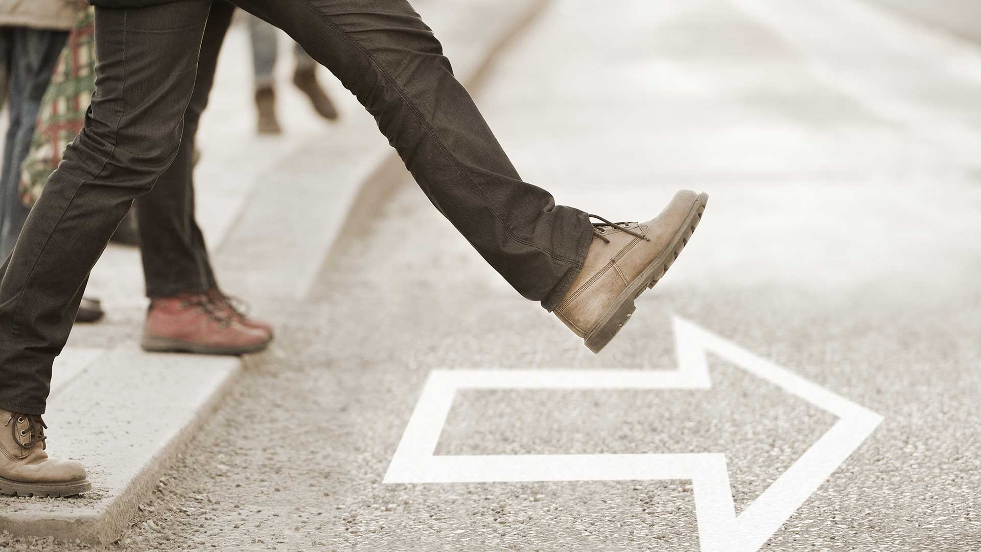 A person wearing boots steps boldly out into the road, following the direction of a painted arrow.